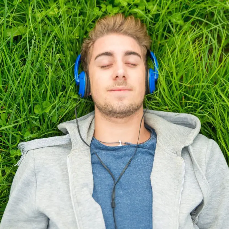 Man ligt ontspannen in het gras met gesloten ogen en koptelefoon, symbool voor rust, ontspanning en mentale ontspanning in de natuur.